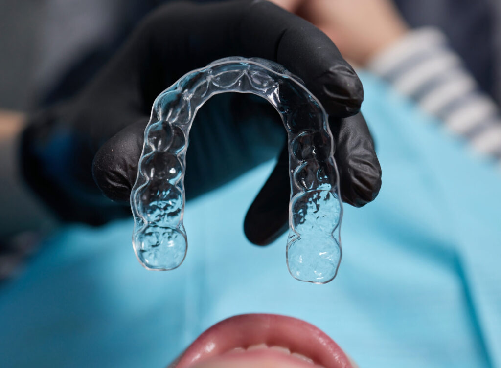 caucasian little kid girl invisible aligner and pointing to her perfect straight teeth. Dental healthcare and confidence concept.