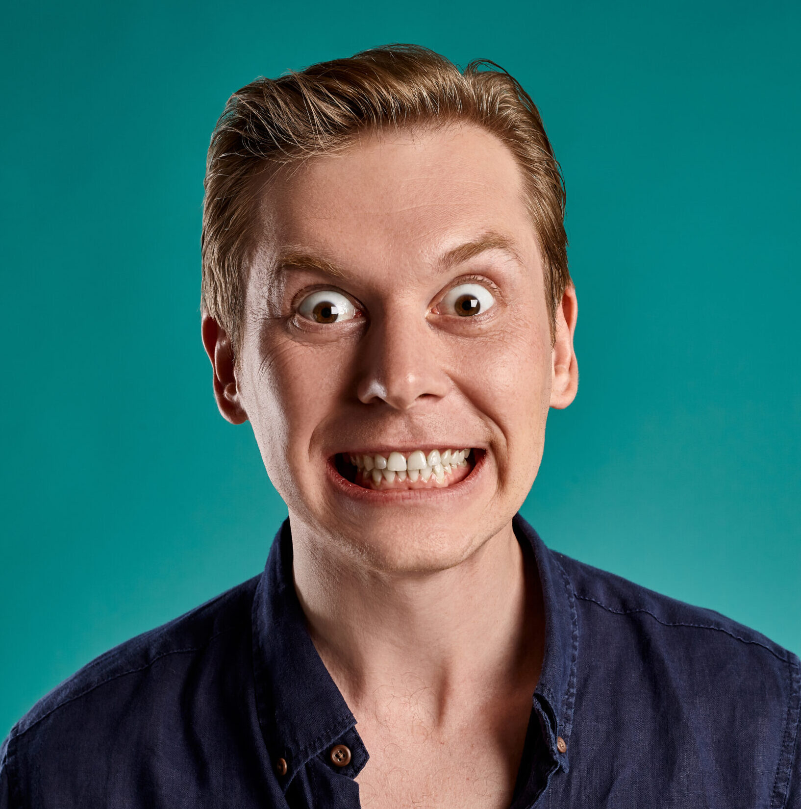 Close-up portrait of a ginger guy in navy t-shirt posing on blue background. Sincere emotions.